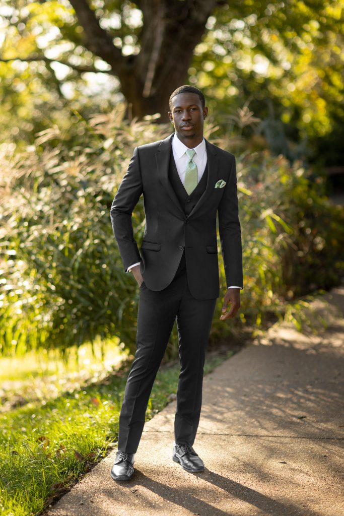 Model posing among greenery in a black suit with light green accessories