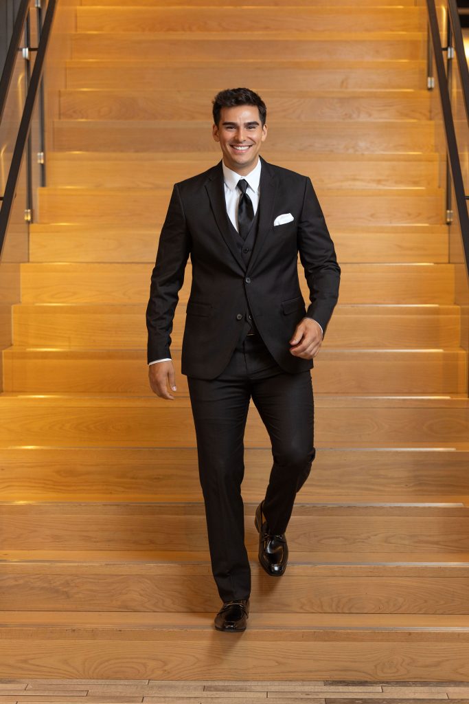Model wearing a black stretch suit smiling walking down a flight of stairs.